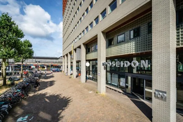 Entree van het Poseidon-gebouw aan het Johanna Westerdijkplein met fietsenstalling en voorbijgangers op de voorgrond.